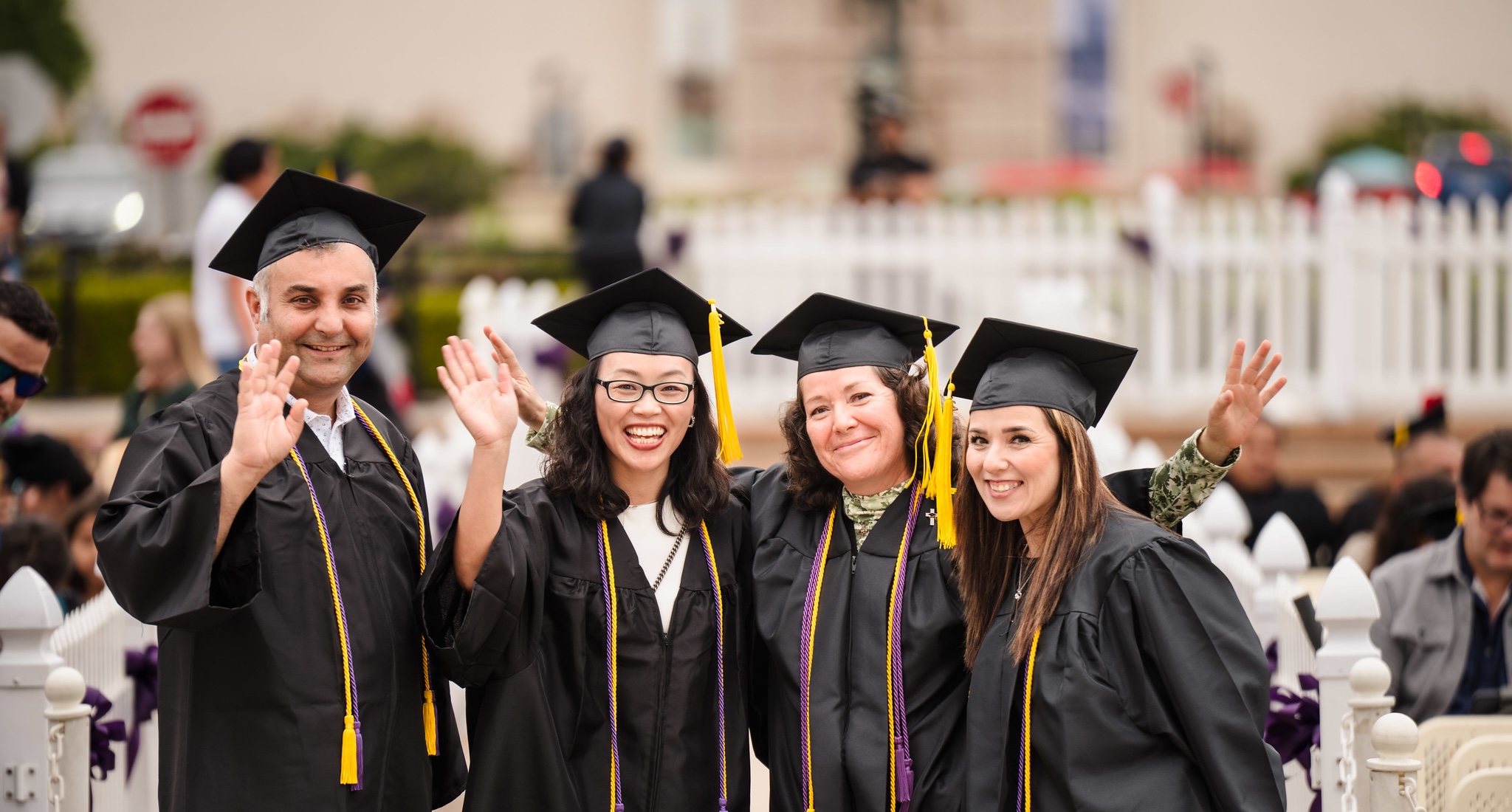 Four SDCCE graduates smiling and waving at commencement